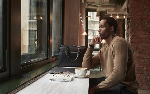 Man sat at a window with a leather bag and laptop