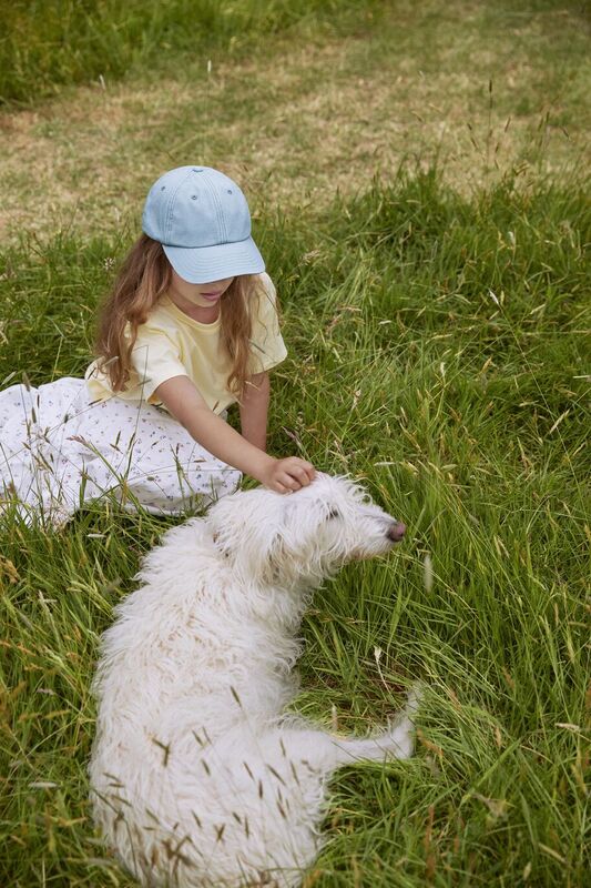 A girl wearing a Beechfield cap lying down in a field petting a dog