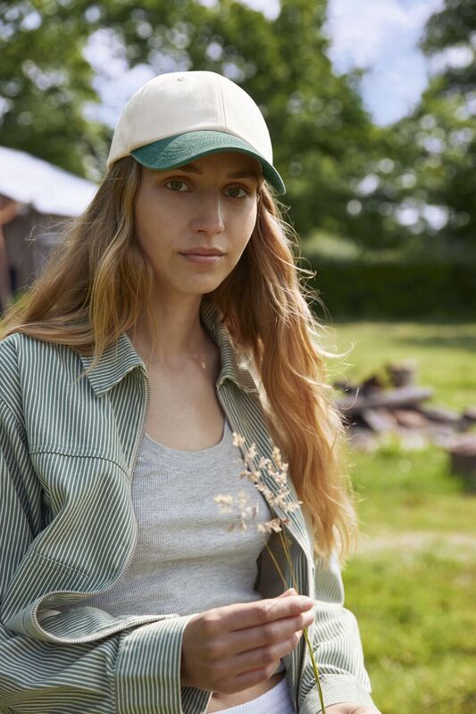 A woman wearing a beechfield cap holding a single flower