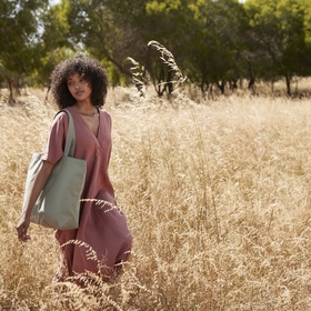 A woman walking through a field wearing a tote bag